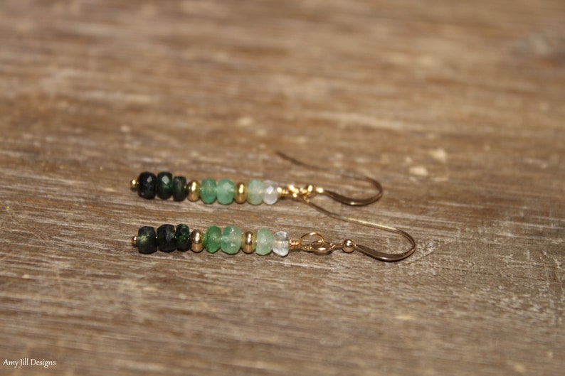 May include: A pair of gold earrings featuring a gradient of green gemstone beads. The beads range from dark green to light green.