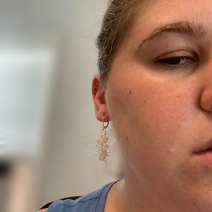 Peut inclure: Une paire de boucles d'oreilles pendantes en argent avec des perles blanches. Les boucles d'oreilles pendent du lobe de l'oreille d'une personne.