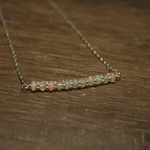May include: A silver chain necklace with a row of small, iridescent opal beads.