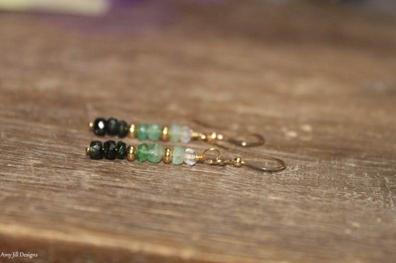 May include: A pair of green and black gemstone earrings with gold accents. The earrings are made with a variety of green and black gemstones, including emerald, peridot, and onyx. The earrings are finished with gold-plated hooks.
