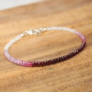 May include: A delicate bracelet made with faceted gemstone beads. The beads are a gradient of white, pink, and red. The bracelet is secured with a silver clasp.