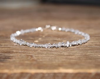 Puede incluir: Una pulsera delicada compuesta por numerosos fragmentos pequeños de cristal transparente en bruto, ensartados en una banda circular continua. Los cristales tienen bordes irregulares y dentados con un aspecto translúcido que refleja la luz.