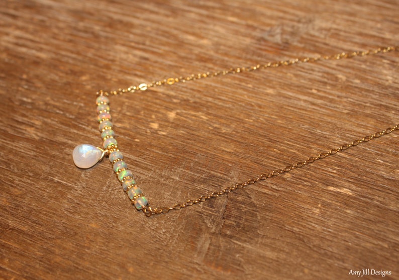 May include: A delicate gold necklace with a bar of opal beads and a pear-shaped moonstone pendant. The necklace is on a wooden surface. The chain is approximately 45 cm long.