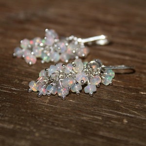 Peut inclure: Une paire de boucles d'oreilles pendantes en argent avec un groupe de pierres d'opale blanches iris&eacute;es.