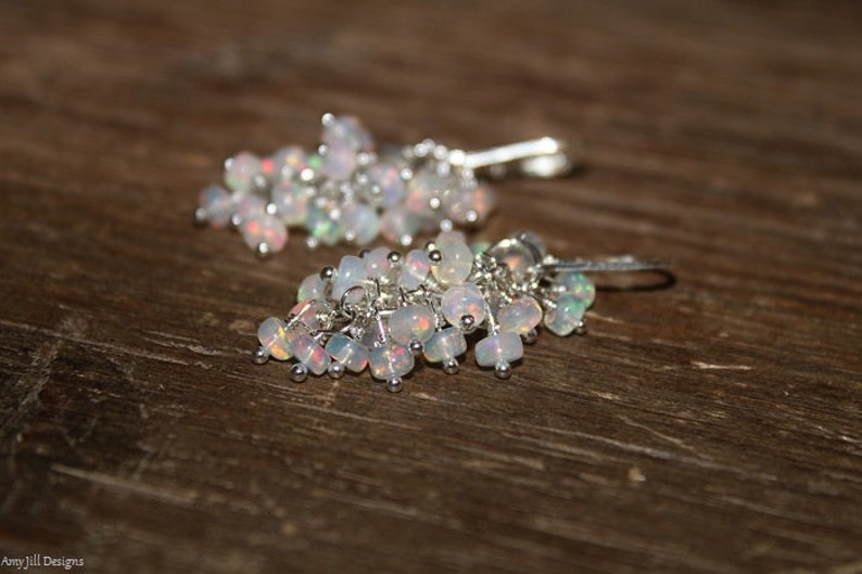 Peut inclure: Une paire de boucles d'oreilles pendantes en argent avec un groupe de pierres d'opale blanches iris&eacute;es.