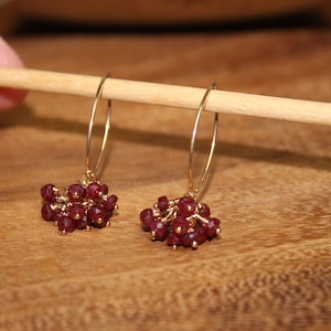 May include: A pair of gold hoop earrings with dangling clusters of small, faceted, dark red gemstones.