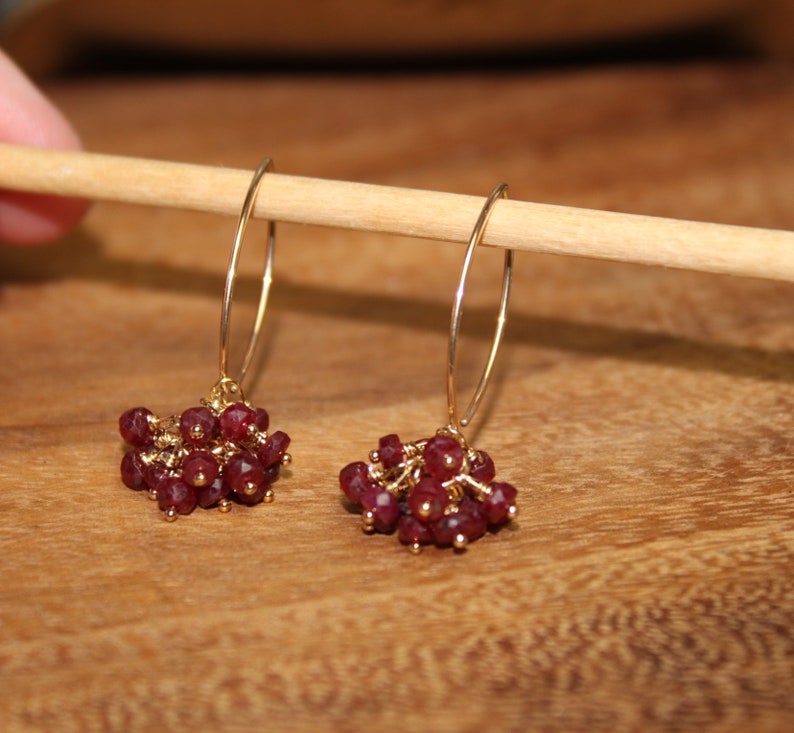 May include: A pair of gold hoop earrings with dangling clusters of small, faceted, dark red gemstones.