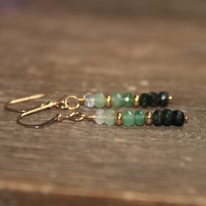 May include: A pair of gold dangle earrings with a gradient of green and black gemstone beads.