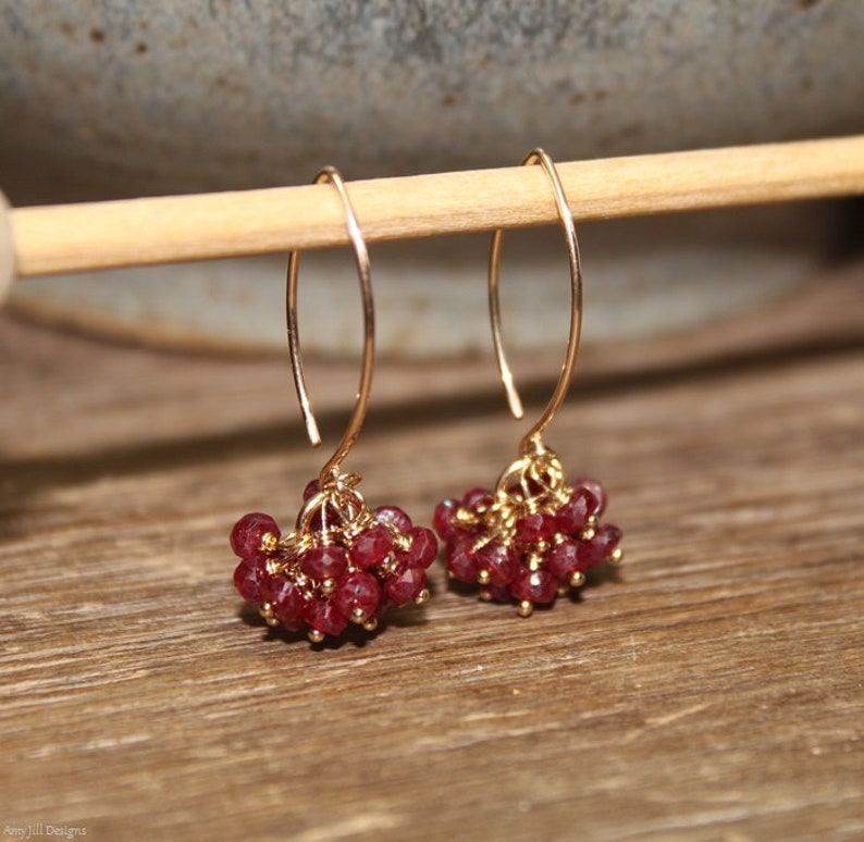 May include: Gold dangle earrings with a cluster of small, red gemstone beads.