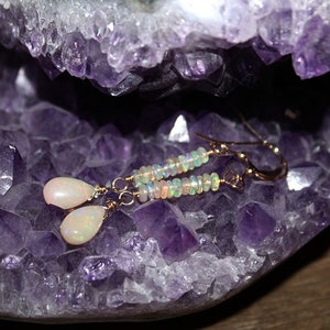 Puede incluir: Pendientes dorados con colgantes de &oacute;palo en forma de l&aacute;grima y detalles de cuentas. Los pendientes se exhiben sobre una geoda de amatista p&uacute;rpura. La joyer&iacute;a tiene un dise&ntilde;o delicado y es adecuada para el uso diario o ocasiones especiales.