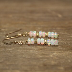 May include: A pair of gold earrings with white opal beads. The earrings are dangle style with a small gold bead at the top of each earring.