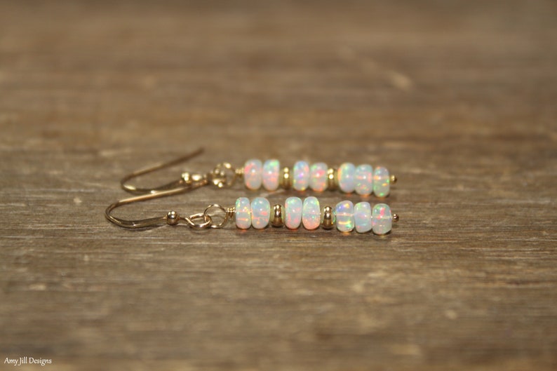 May include: A pair of gold earrings with white opal beads. The earrings are dangle style with a small gold bead at the top of each earring.