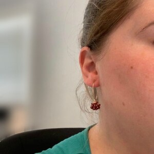 May include: Gold hoop earrings with a cluster of small red gemstones dangling from the bottom.