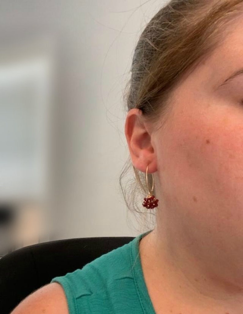 May include: Gold hoop earrings with a cluster of small red gemstones dangling from the bottom.