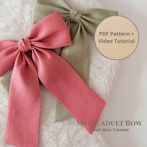 May include: Two large linen bows, one in a dusty rose color and the other in a muted green. The bows are on a white, textured surface. Text on the image reads "PDF Pattern + Video Tutorial" and "Marie Adult Bow Linen Bow Tutorial."