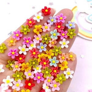 May include: A collection of small, colorful flower-shaped embellishments in various shades of pink, red, yellow, green, and blue. Each flower has a contrasting center, creating a vibrant and cheerful appearance. These decorative elements are ideal for crafts.