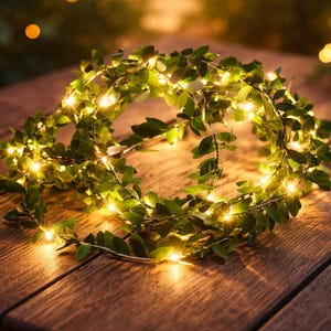 May include: A circular garland of green leaves with small, warm white LED lights. The garland is arranged on a wooden surface, creating a soft, inviting glow. Ideal for home decor or festive occasions.