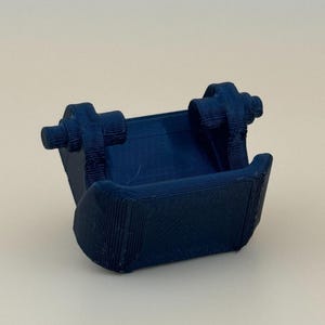 May include: A dark blue 3D printed component featuring a central rectangular bucket-like section with two protruding cylindrical hinge mounts on the top sides, characterized by visible horizontal layer lines from the additive manufacturing process.