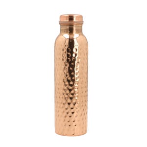 Könnte beinhalten: Eine Kupfer-Wasserflasche mit gehämmerter Oberfläche. Die Flasche ist rund und hat einen Schraubverschluss.