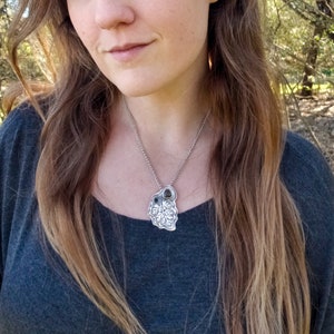 Pu&ograve; includere: Una collana d'argento con un ciondolo a forma di foglia dettagliato con due pietre verde scuro. La collana &egrave; indossata da una persona con i capelli lunghi e castani.