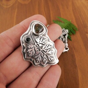 Pu&ograve; includere: Un ciondolo d'argento con un designo a foglia dettagliato e due pietre preziose. La pietra pi&ugrave; grande &egrave; un diaspro verde e marrone, e la pietra pi&ugrave; piccola &egrave; un onice nero.