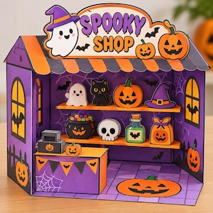 Peut inclure: Un ensemble de jeu en carton sur le thème d'Halloween avec un schéma de couleurs violet et orange. La structure comprend des étagères présentant des découpes miniatures d'un fantôme, d'un chat noir, d'une citrouille, d'un chapeau de sorcière.