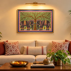 May include: A rectangular wall painting featuring two black elephants facing each other under a large green tree, framed in gold. The artwork includes intricate patterns in red, blue, and yellow, set against a cream-colored wall above a sofa.