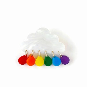 May include: A white cloud-shaped brooch with a rainbow of colorful raindrops hanging from it.