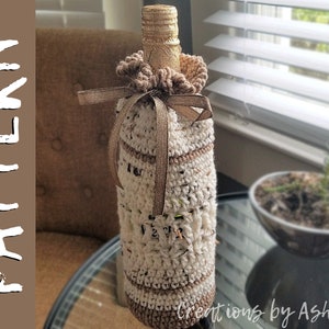 May include: A crocheted bottle cozy in white and brown with a gold ribbon. The cozy is made with a textured stitch and has a ruffled top. The bottle is not visible.