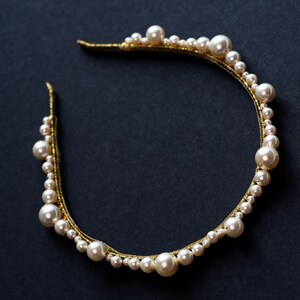 Sculptural pearl and crystal tiara detail on black background.