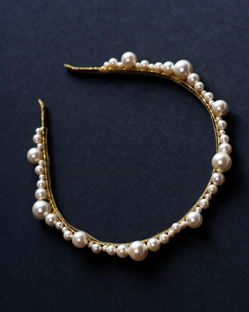 Sculptural pearl and crystal tiara detail on black background.