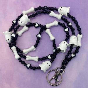 May include: A black and white beaded lanyard with ghost and bone charms. The lanyard has a black heart bead pattern and a silver swivel clip.