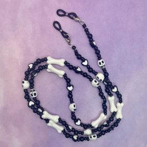 May include: Black and white beaded glasses chain with skull and bone charms. The chain has black heart charms and silver metal clasps.