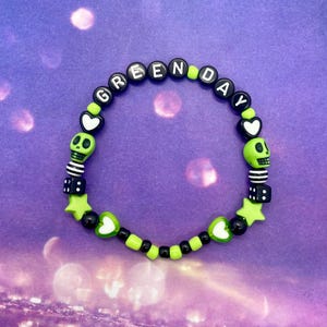 Può includere: Braccialetto con perline con teschi bianchi e neri, dadi, cuori e stelle. Le perline compongono la scritta "Green Day" in lettere nere.