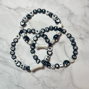 May include: Three black and white beaded bracelets with the words "FLESH", "HOCKY", and "BEINGS" spelled out. The bracelets also feature dice, stars, hearts, and skulls.
