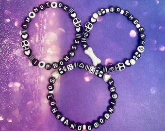 May include: Three beaded bracelets with black and white beads. The bracelets spell out phrases like "I PROMISE", "MONOTOK", and "SO LONG AND GOOD NIGHT". The bracelets feature skull, heart, and cross charms.