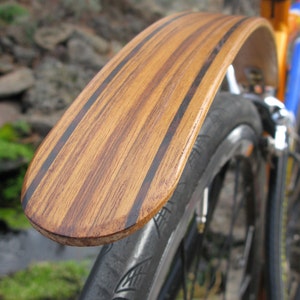 May include: A wooden bicycle fender with a striped pattern. The fender is attached to a black bicycle tire.
