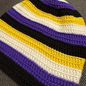 Op de afbeelding: Een gebreide beanie met strepen in paars, wit, geel en zwart.
