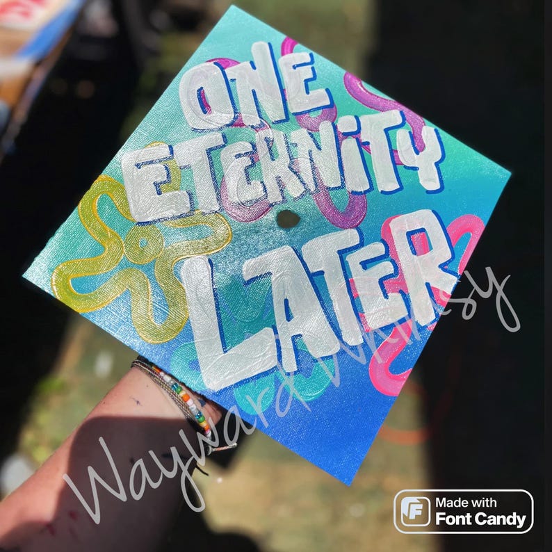May include: A blue graduation cap with a white and yellow design. The cap has the words "One Eternity Later" written on it.