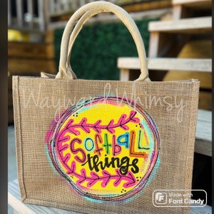 May include: A brown burlap tote bag with a yellow circle and colorful design that says "Softball Things".