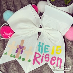 May include: White bow with a purple heart and three crosses with the text "He is Risen" in colorful letters.