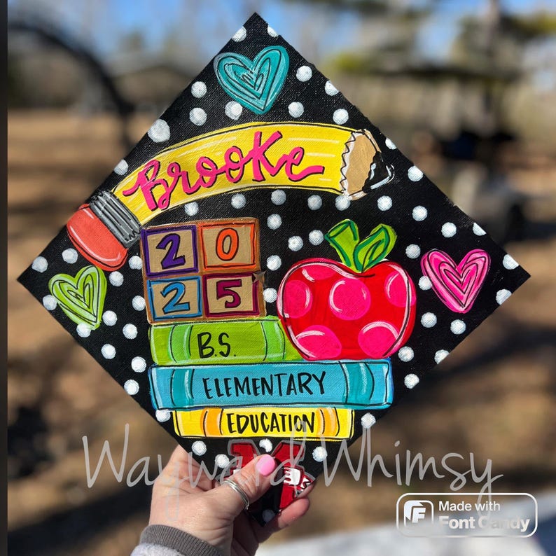 May include: A black graduation cap decorated with a colorful design. The cap features a yellow pencil, a stack of books, a red apple, and a block with the numbers 2025. The text "Brooke" is written in pink on the cap.