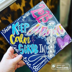 May include: A blue graduation cap painted with a medical caduceus, wings, and the text "Keep Calm & Scrub In". The cap also includes the names "Chasity", "Justin", "Evan", "Sadie", and "SAB".