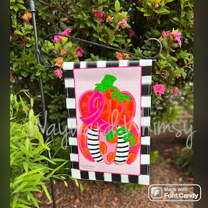 May include: A garden flag featuring a pink and orange pumpkin design with the words "Wayward Whimsy". The pumpkin has a green stem and black and white striped accents. The flag is bordered with a black and white checkered pattern.