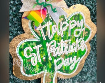 May include: A green shamrock-shaped sign with gold accents and the text "Happy St. Patrick's Day" written in white. The sign is decorated with a rainbow ribbon.