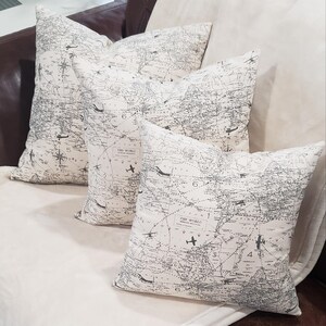 May include: Three decorative throw pillows with a white background and a black and gray world map print. The pillows feature a vintage airplane design and the text "The World".