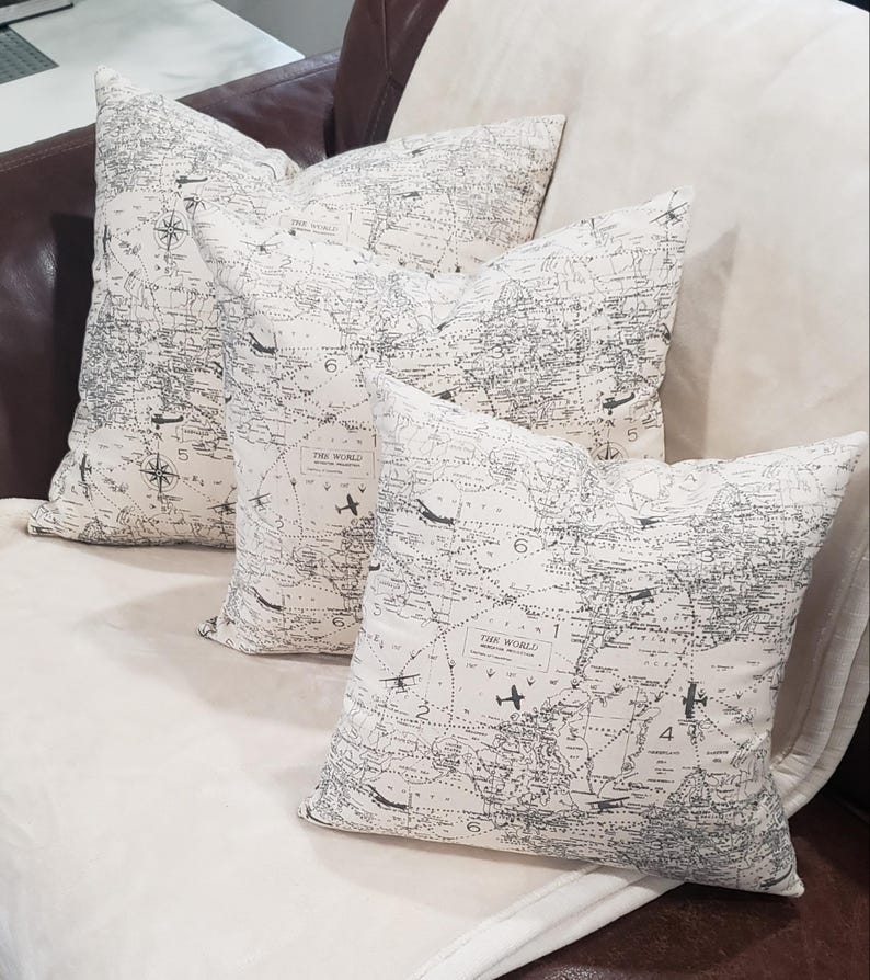 May include: Three decorative throw pillows with a white background and a black and gray world map print. The pillows feature a vintage airplane design and the text "The World".