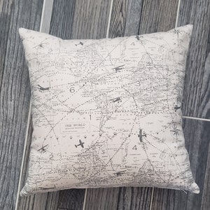 May include: A beige throw pillow with a black and white world map print. The map features airplane illustrations and the text "The World Mercator Projection".