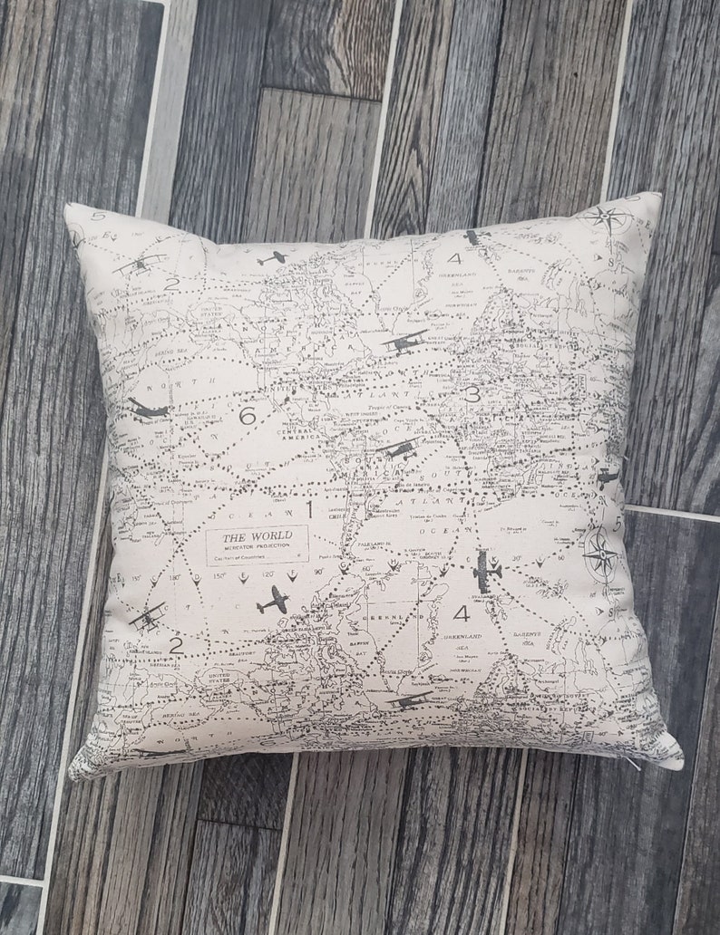 May include: A beige throw pillow with a black and white world map print. The map features airplane illustrations and the text "The World Mercator Projection".