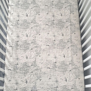 May include: A white crib sheet with a black and white airplane and compass print. The sheet has a vintage map design.